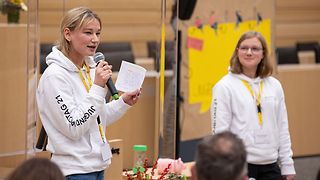 Junge Moderatorin mit Mikrofon und Karteikarten