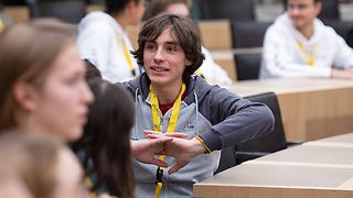 Jugendlicher sitzt im Plenarsaal mit Landtags-Schlüsselband