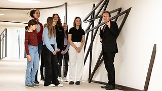 Ein Mitarbeiter des Besucherdienstes steht mit Schülerinnen im Verbindungstunnel des Landtagsgebäudes und erklärt etwas.