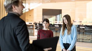 Zwei Schülerinnen hören dem Mitarbeiter des Besucherdienstes zu.