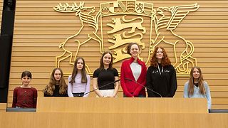 7 Schülerinnen stehen vor dem Landeswappen im Plenarsaal.