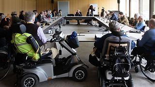 Menschen mit und ohne Behinderung an einem Thementisch im Sitzungssaal.
