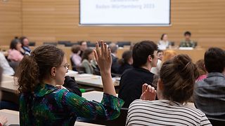Publikum im Plenarsaal, eine Zuhörerin meldet sich