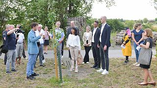 Landtagspräsidentin Muhterem Aras, Jugendguide Benjamin und weitere vor einem gepflanzten Apfelbaum am Mahnmal in Hailfingen