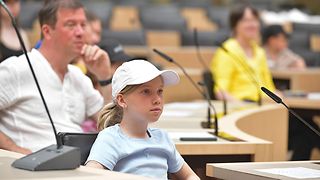 Ein Mädchen sitzt im Plenarsaal.
