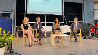 Aras spricht auf auf der Bühne mit Schülerinnen und Schülern