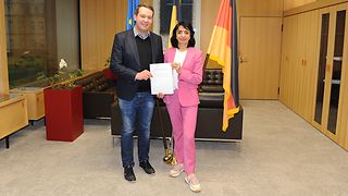 Muhterem Aras und Oliver Hildenbrand halten den Halbzeitbericht des Gremiums in den Händen.
