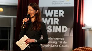 Autorin Nicole Köster spricht vor einem Aufsteller mit der Aufschrift "Wer wir sind".