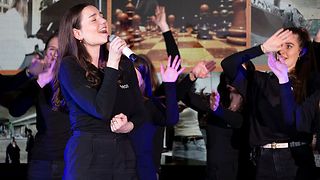 Eine Studentin singt, weitere schwenken die Arme auf der Bühne.