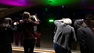 Besucherinnen schauen in den bunt beleuchteten Plenarsaal.