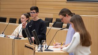 Debattierende im Plenarsaal machen sich schriftliche Notizen