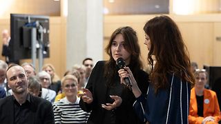 Moderatorin Köster hält ein Mikrofon vor eine Schülerin im Publikum.