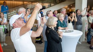 Besucher in der Lobby des Landtagsgebäudes verfolgen einen Beitrag auf der Bühne
