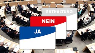Die Stimmkarten Ja, Nein und Enthaltung vor dem Hintergrund mit Abgeordneten im Plenarsaal