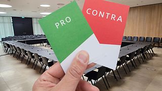 Stimmkarten Pro und Kontra vor dem Hintergrund eines Sitzungssaals