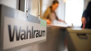 Schild Wahlraum mit Blick in ein Wahllokal