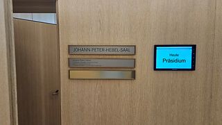 Türe und Belegungsdisplay eines Konferenzsaales mit Text "Heute Präsidium"