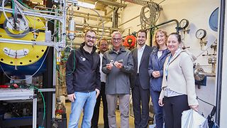 Gruppenbild von Landtagspräsident Strobl, der Abgeordneten Isabell Huber und Vertreterinnen und Vertretern des DLR in einem Prüfstand.