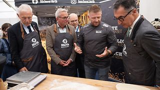 Mergel, Strobel, Bäcker Hirth und Özdemir vor einer mit Mehl bestäubten Arbeitsplatte