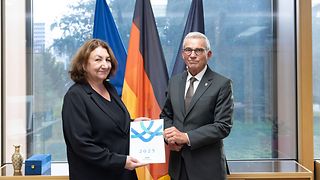 Beate Böhlen übergibt ihren Tätigkeitsbericht an Thomas Strobl vor den Flaggen