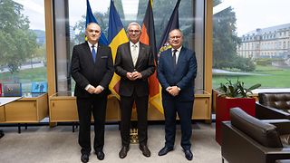 Dr. Vlad Vasiliu, Generalkonsul von Rumänien, Landtagspräsident Thomas Strobl und der rumänische Abgeordnete Ovidiu Victor Gant vor den Flaggen