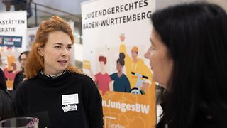 Eine Vertreterin der Jugendarbeit informiert eine Abgeordnete zu ihrer Arbeit. Im Hintergrund sind Infobanner zu sehen.